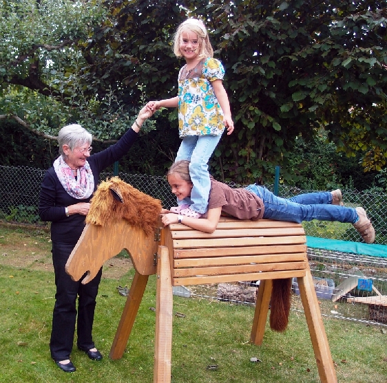 2 Kinder auf einem Holzpferd, das eine hält die Hand der Wunschoma